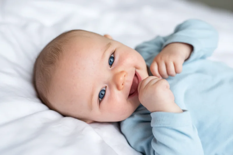 Smiling baby lying on white bed wearing light blue onesie