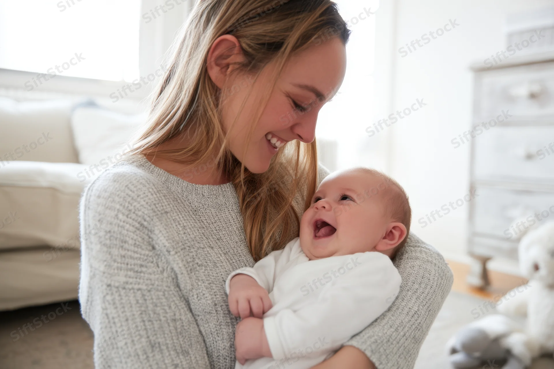 Mother smiling while cradling a laughing baby in a bright living room