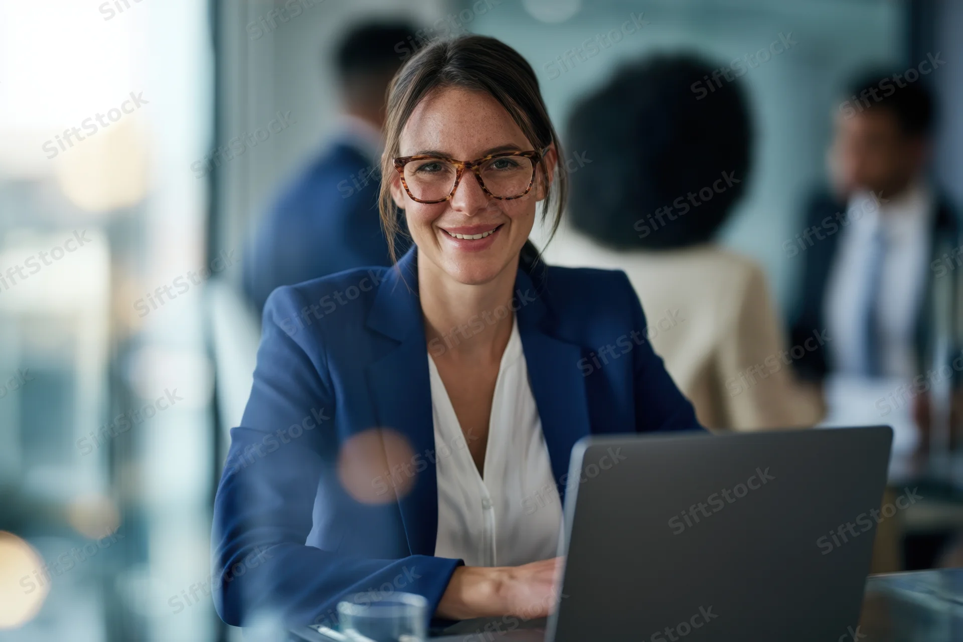 Woman in blue blazer smiling at laptop in modern office setting