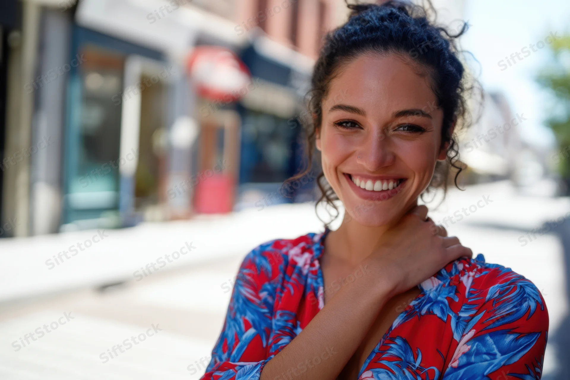 Smiling woman in floral blouse touching her neck on city sidewalk