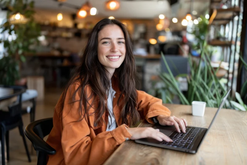Smiling woman working on laptop at wooden table in cafe