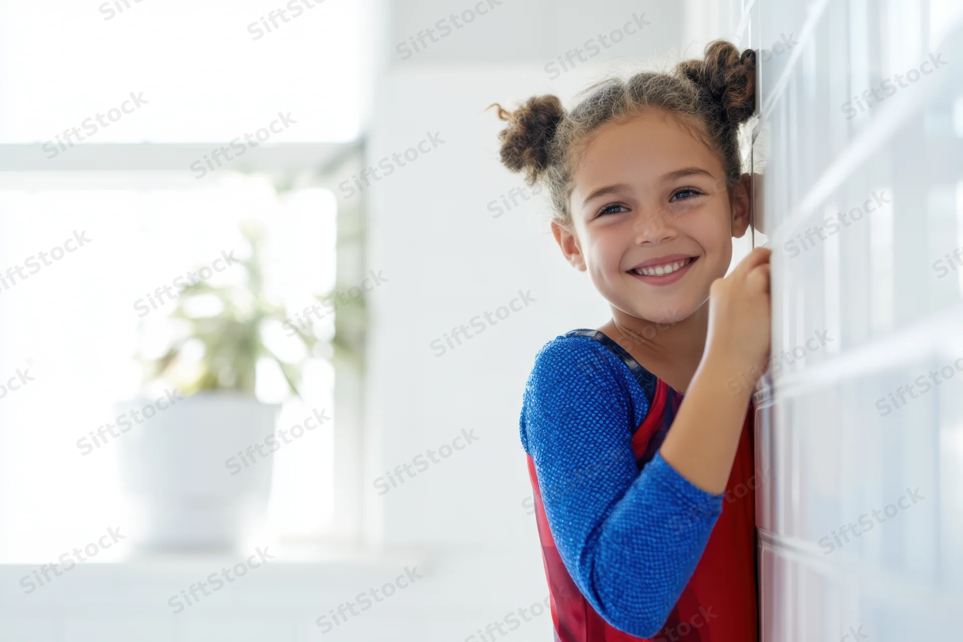 Young girl in blue and red gymnastics leotard smiling while leaning against a tiled wall indoors