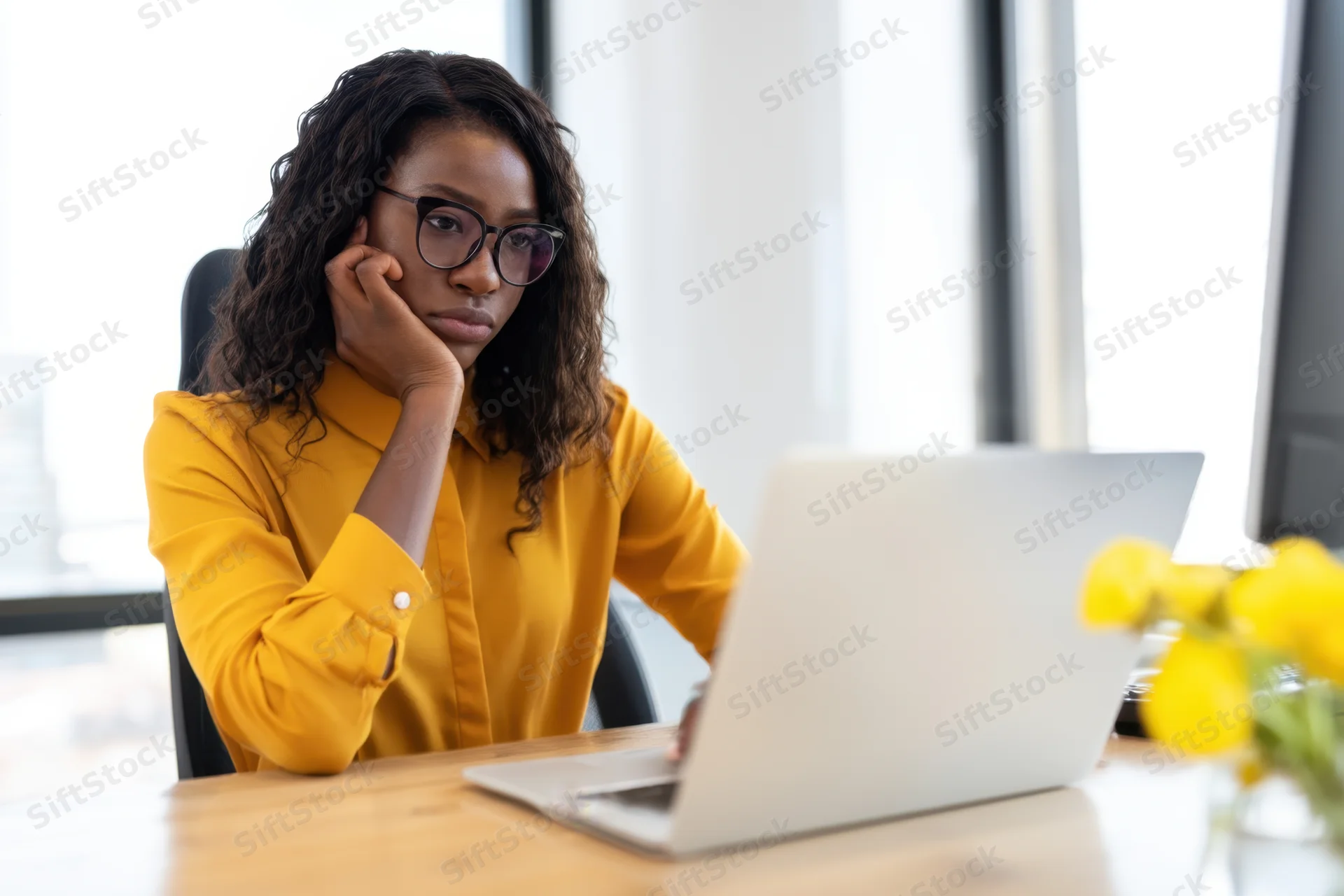 Woman in yellow blouse working on laptop at wooden desk in office