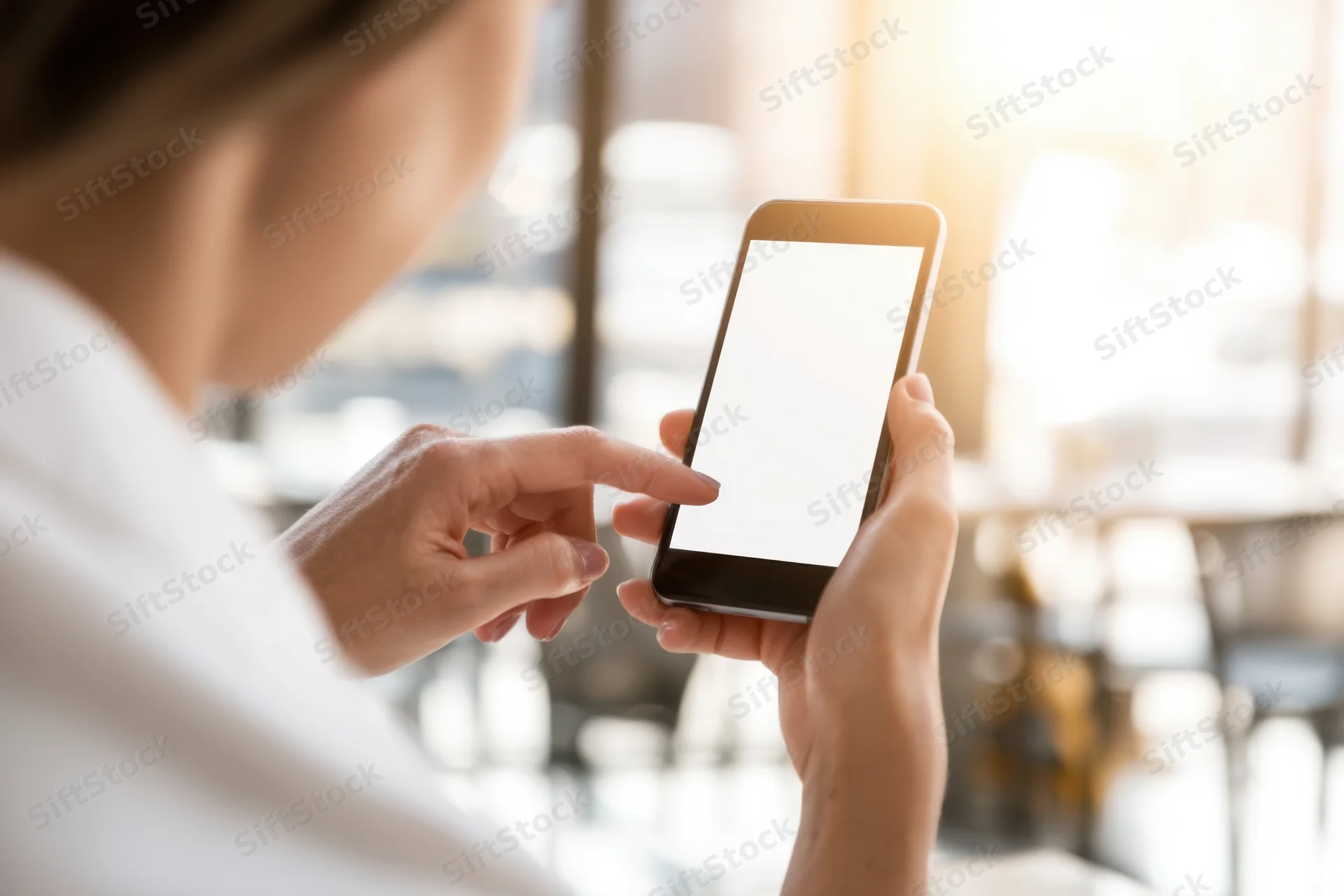 Woman holding smartphone with blank screen in bright cafe interior