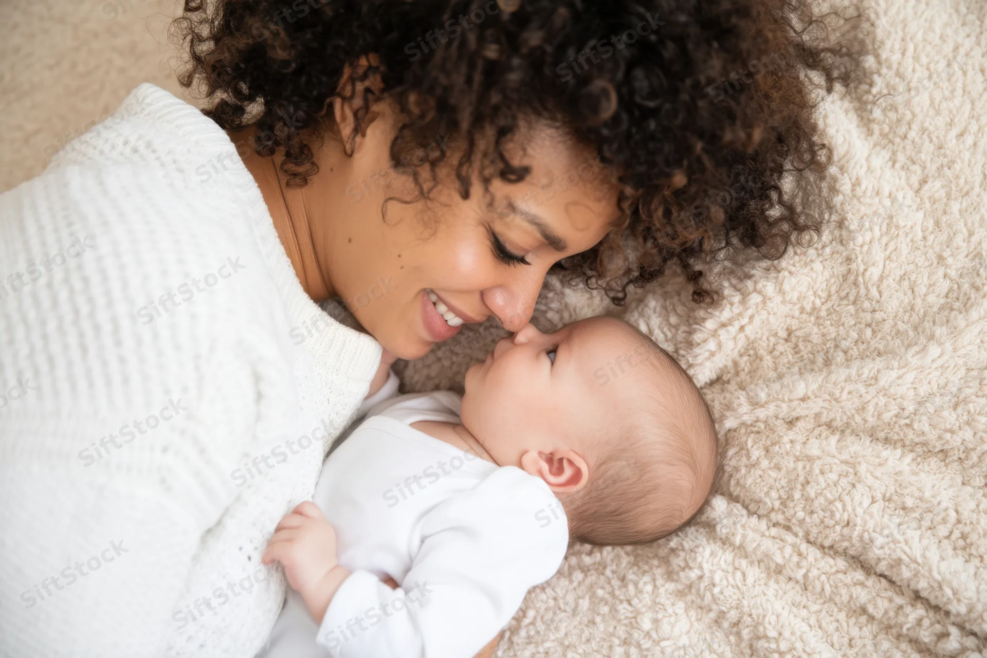 Woman smiling and touching noses with baby while lying on soft blanket