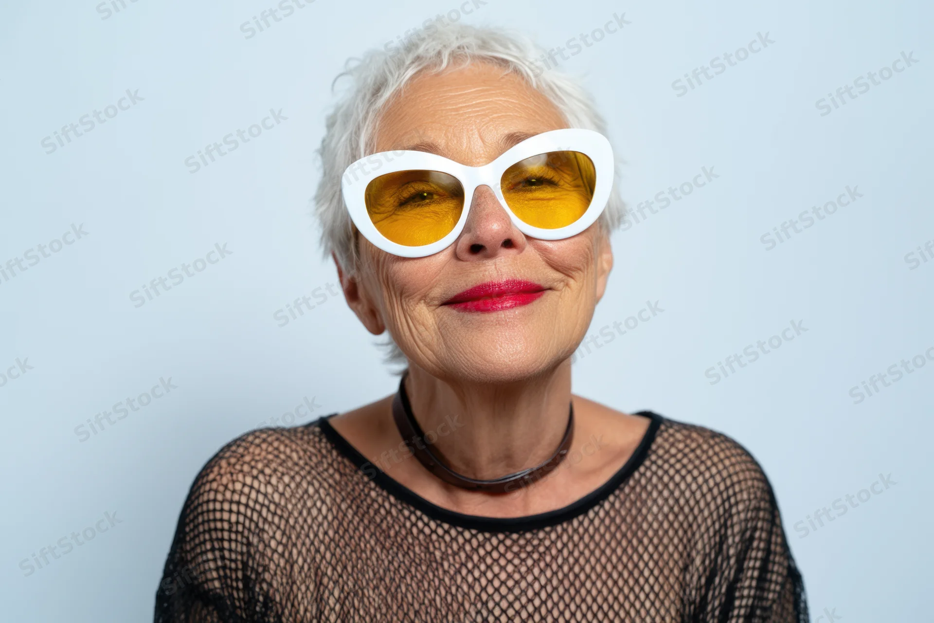 Senior woman with short white hair wearing oversized white cat-eye sunglasses with yellow lenses, smiling confidently in a studio portrait