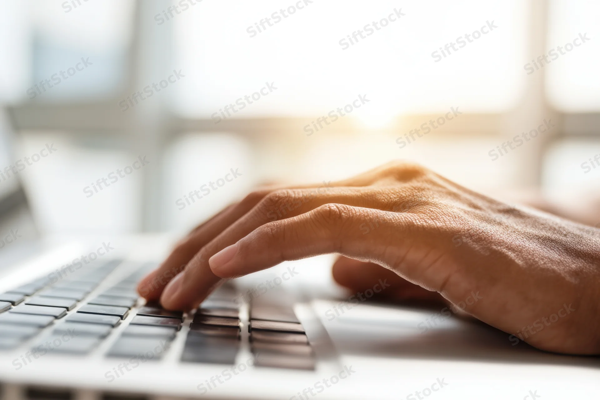 Close-up of hands typing on a laptop keyboard in a sunlit office space