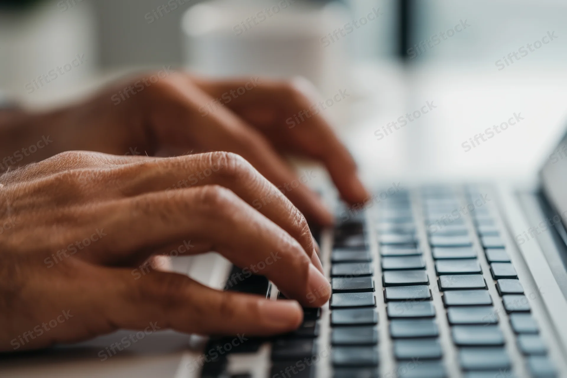 Hands typing on a laptop keyboard in an office setting