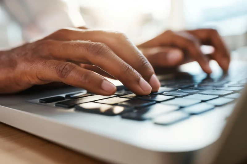 Closeup of hands typing on a laptop keyboard at a desk in natural light