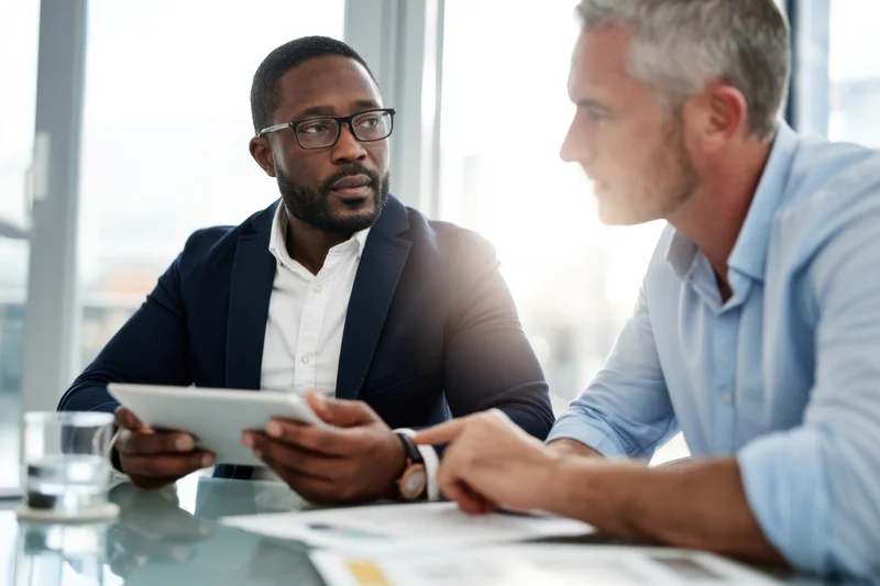 Two businessmen discussing work at a glass table in a modern office