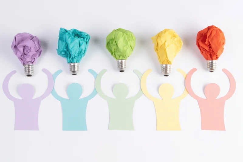 Five colorful paper silhouettes with crumpled paper lightbulbs on heads arranged in a row on white background