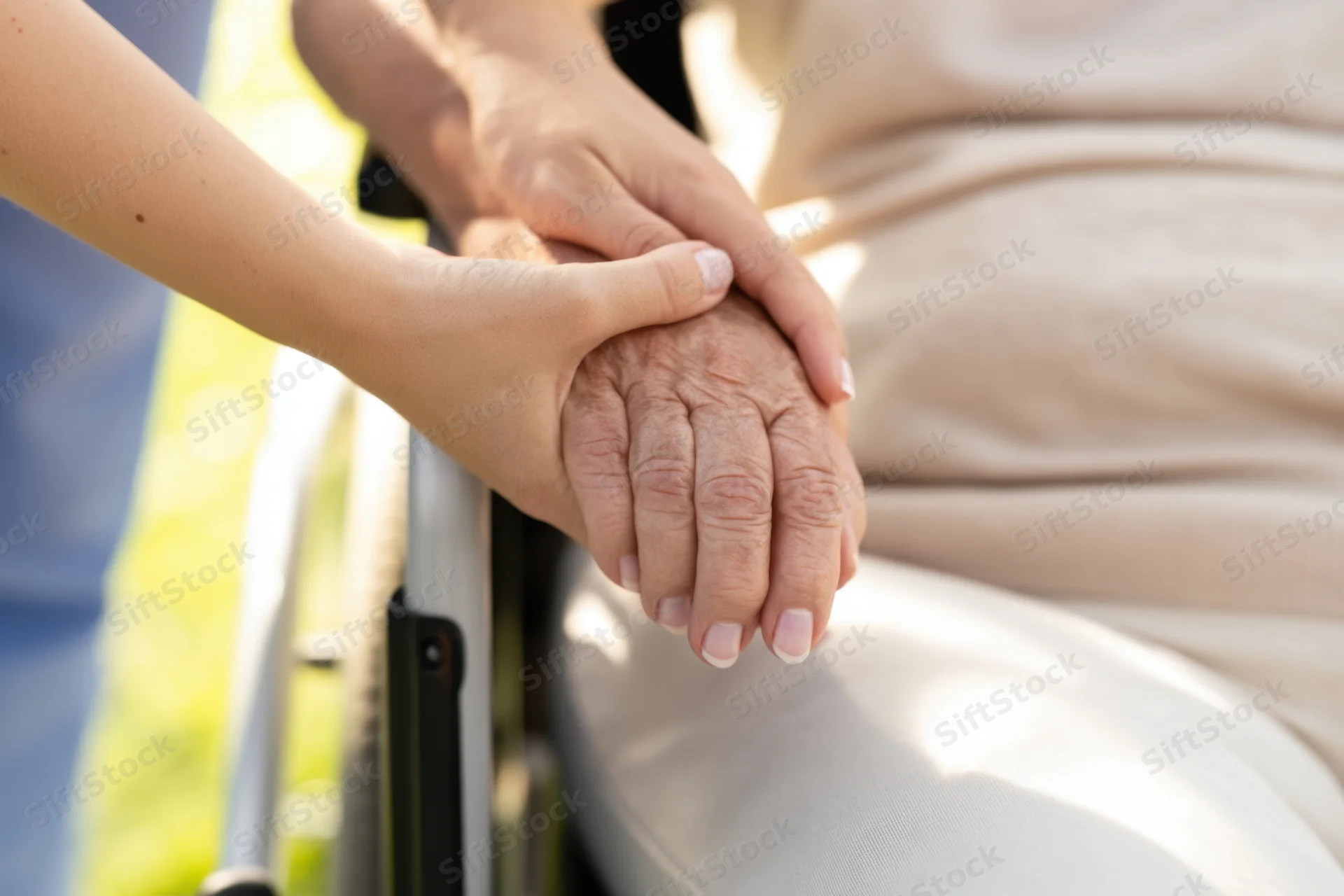 Caregiver’s hands gently holding an elderly person’s hand in a wheelchair