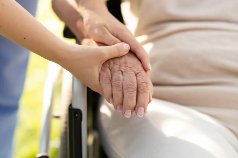 Caregiver’s hands gently holding an elderly person’s hand in a wheelchair