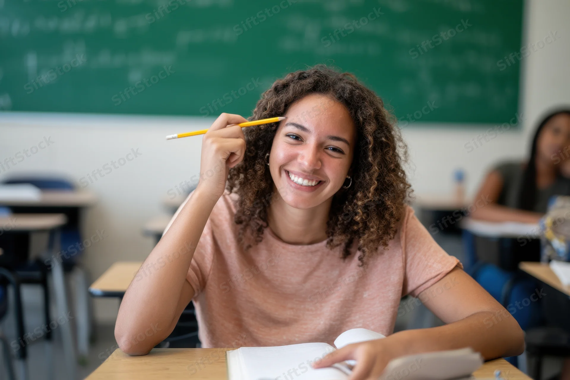 Smiling student holding pencil at desk in classroom