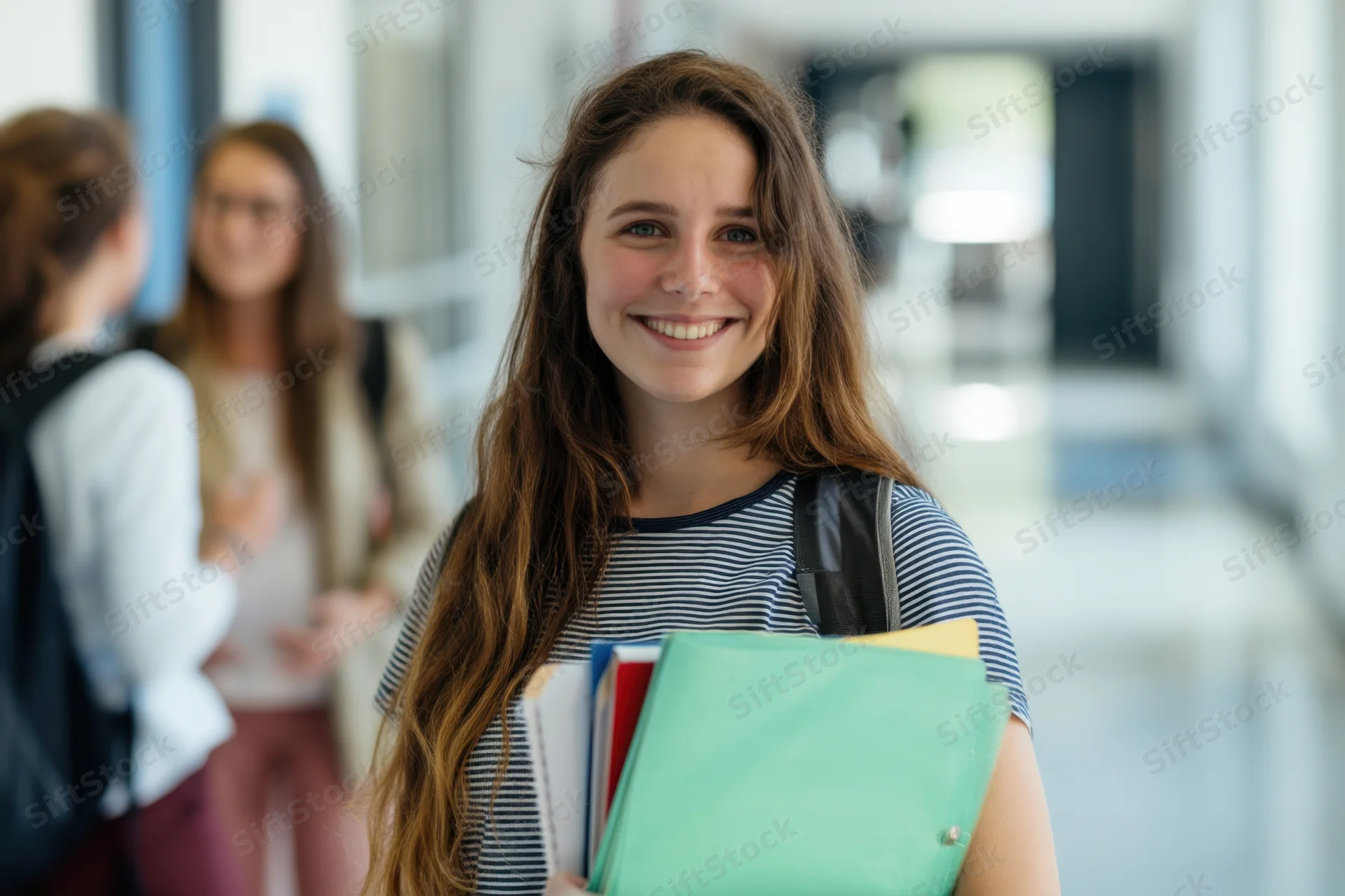 Young woman smiling while holding notebooks and folders in a school hallway