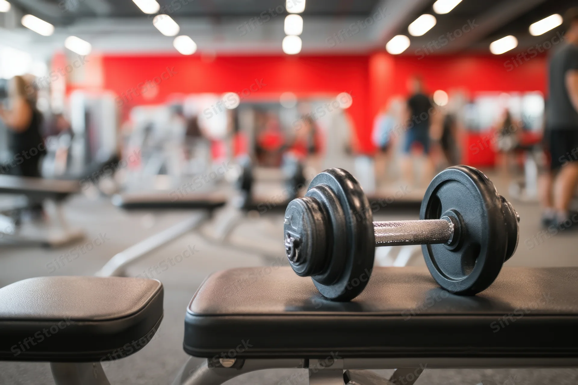 Dumbbell resting on a bench in a gym with red walls and exercise equipment in the background
