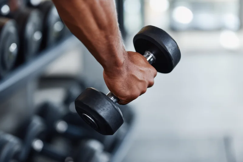 Close-up of a man's muscular forearm gripping a dumbbell in a gym