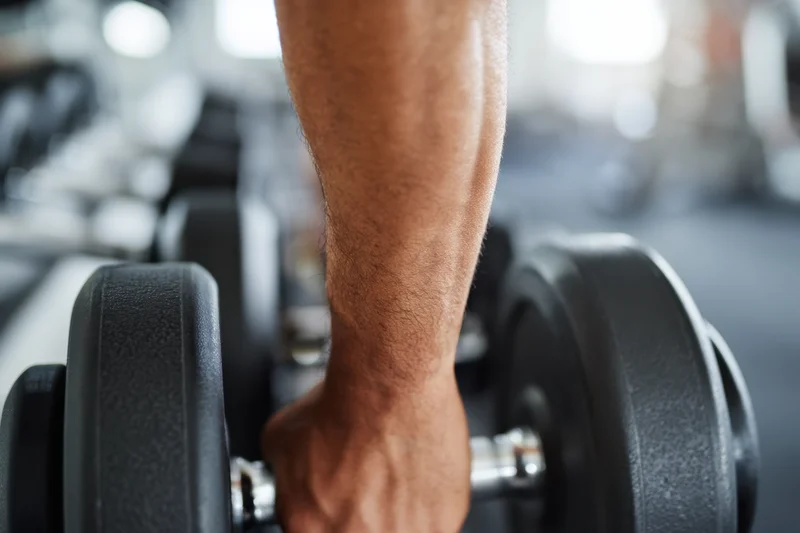 Close-up of a man's forearm gripping a dumbbell in a gym