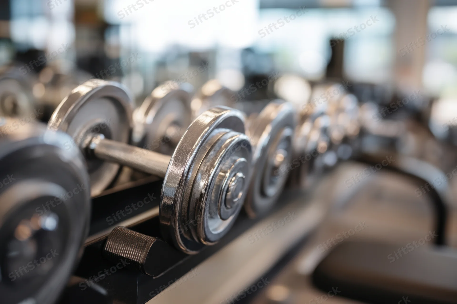 Dumbbells arranged in a row on a gym rack with weight plates visible in the foreground