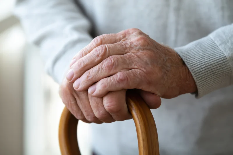 Elderly person's hands gripping a wooden cane for support indoors