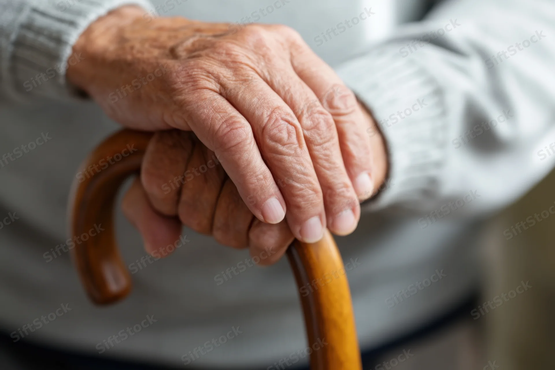 Elderly person's hands gripping a wooden cane for support indoors