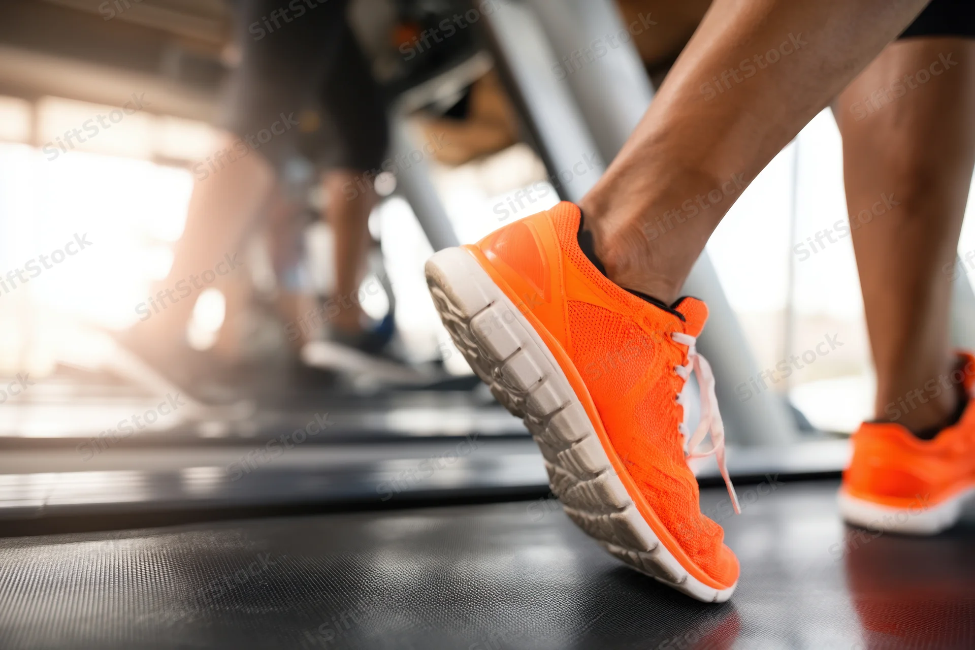 Close-up of bright orange running shoes on a treadmill during a workout in a gym