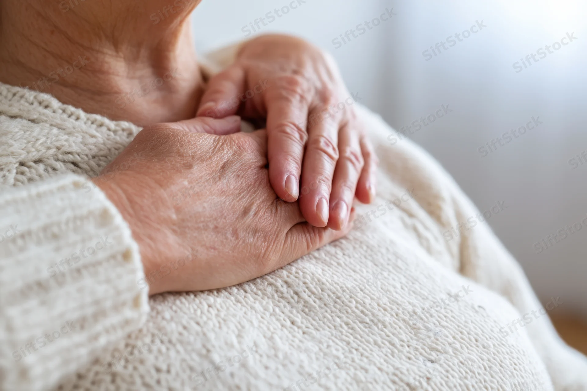 Elderly woman’s hands resting gently on her chest in a knitted sweater