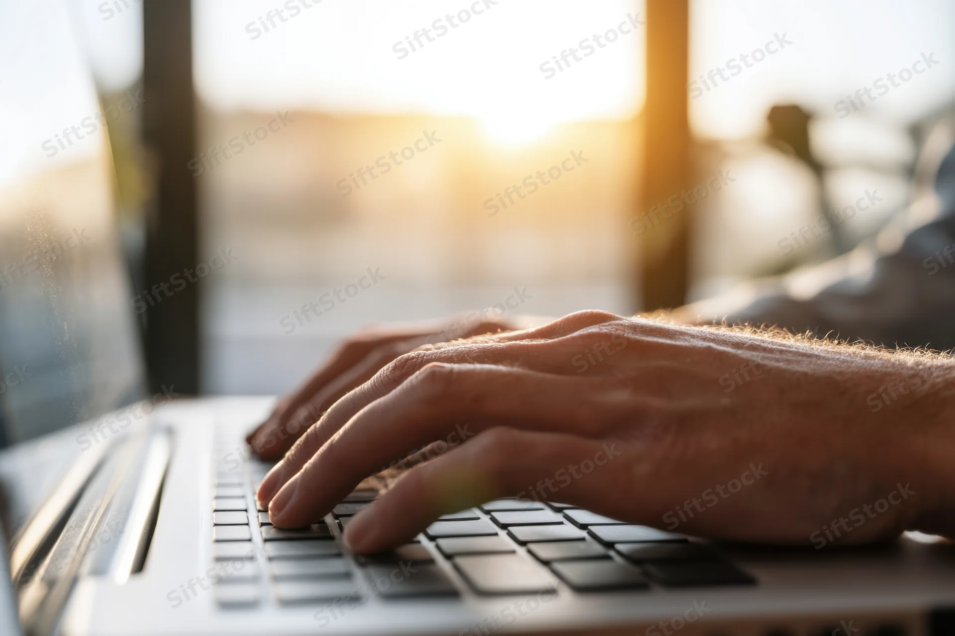Hands typing on a laptop keyboard in warm sunlight at evening