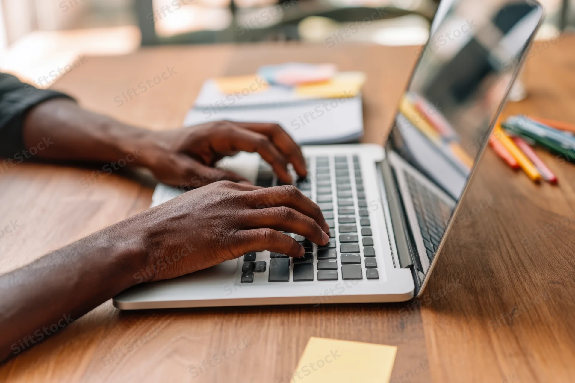 Hands typing on a laptop at a wooden desk in an office workspace