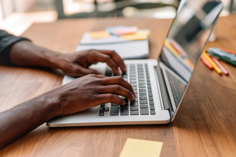 Hands typing on a laptop at a wooden desk in an office workspace