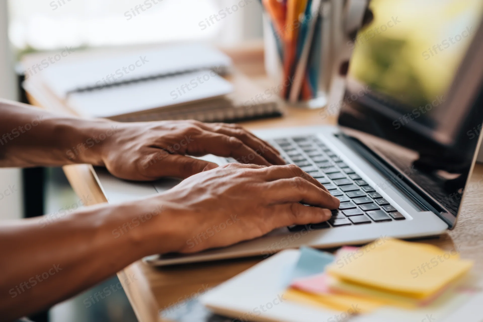 Hands typing on a laptop at a wooden desk in an office workspace