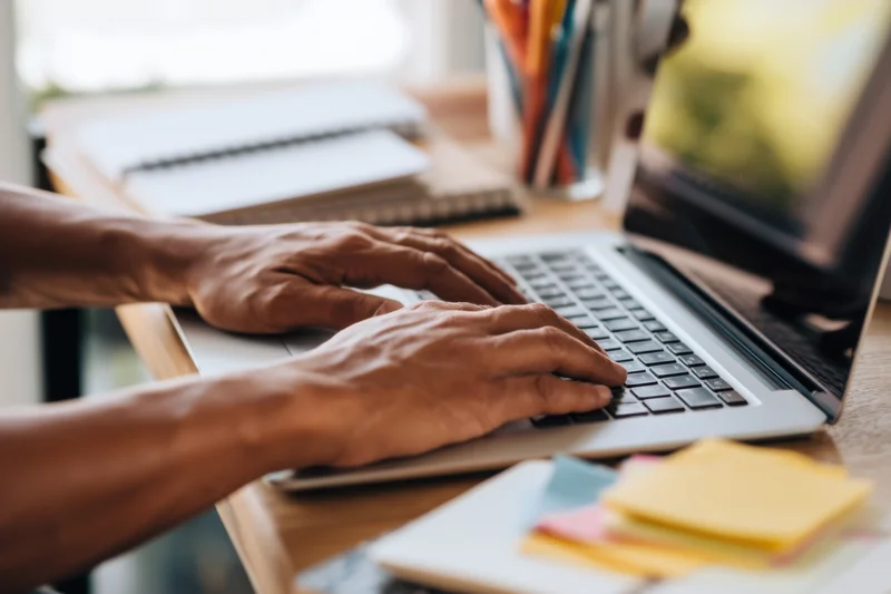 Hands typing on a laptop at a wooden desk in an office workspace