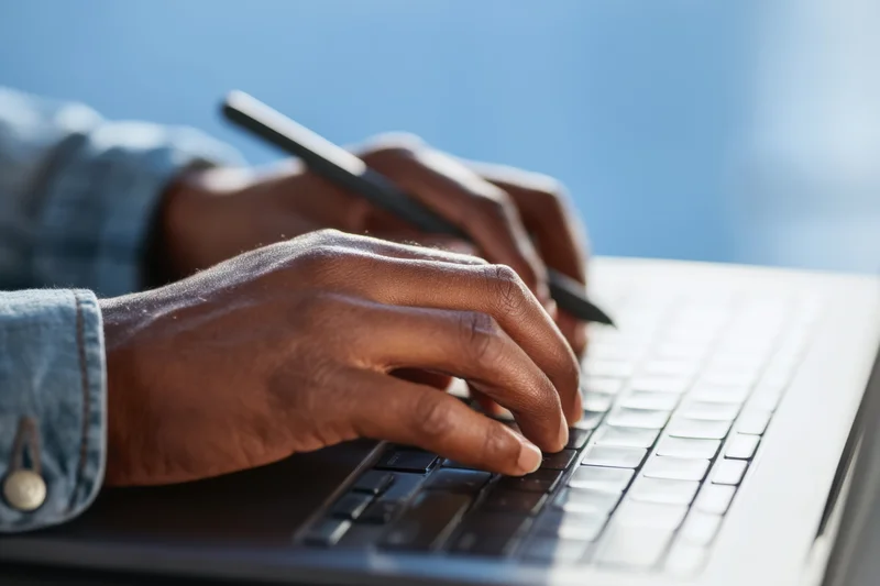 Hands typing on a laptop keyboard with a stylus, close-up view