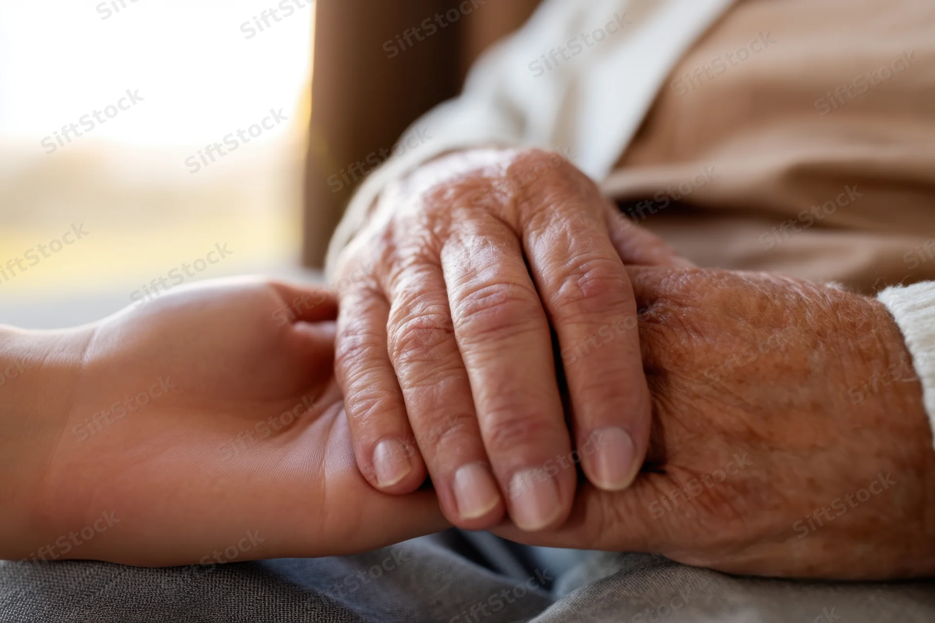 Elderly hand holding a younger hand in a comforting gesture indoors
