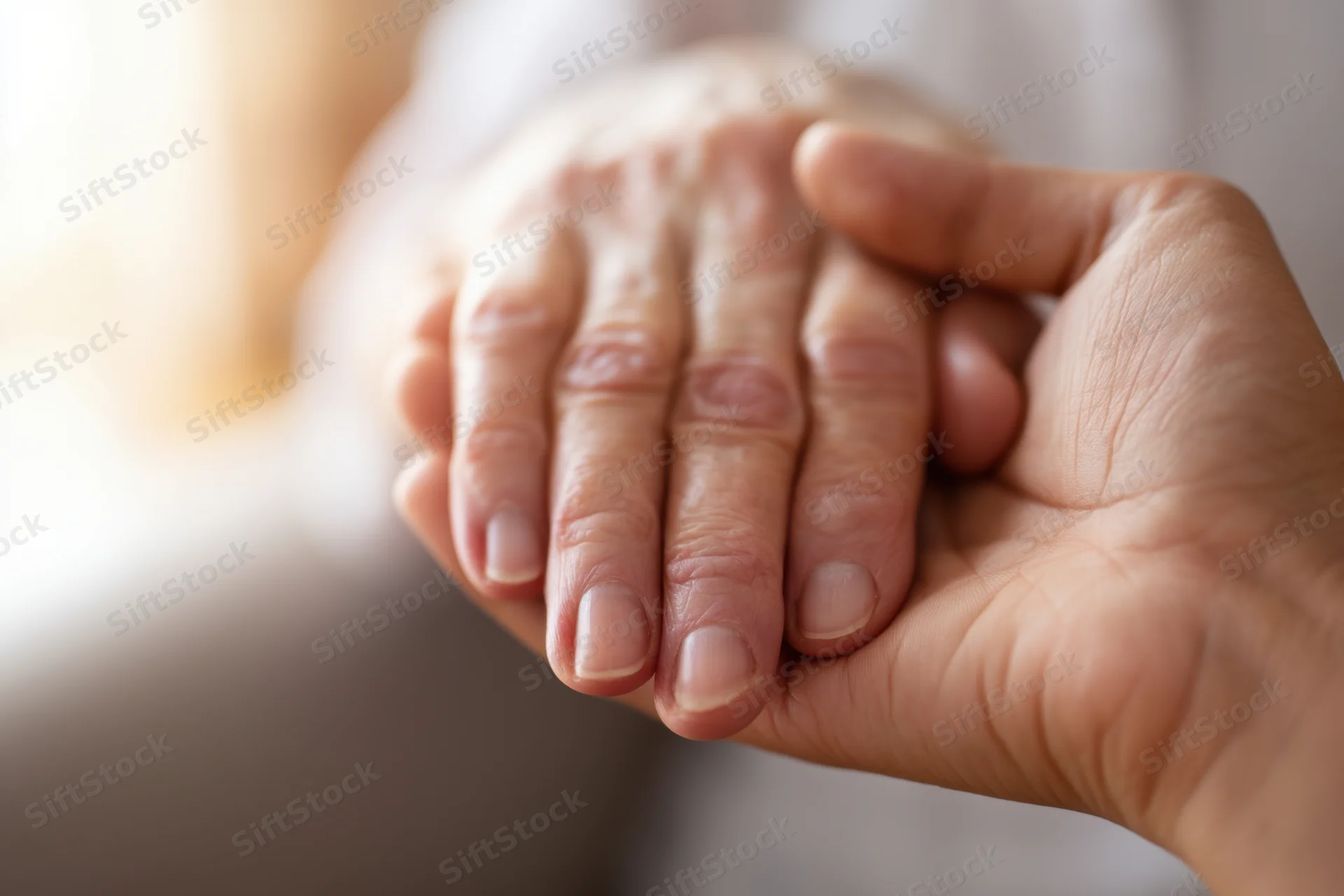 Close-up of two hands clasped in a comforting gesture, one elderly and one younger, showing support and care
