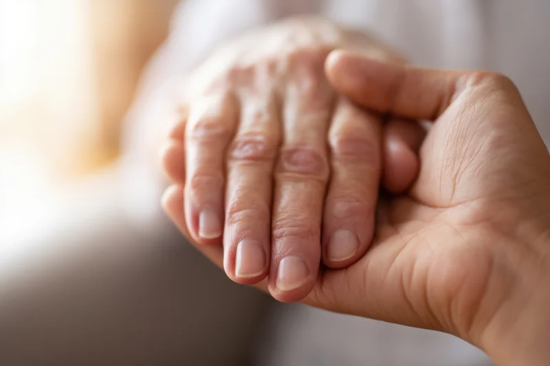 Close-up of two hands clasped in a comforting gesture, one elderly and one younger, showing support and care