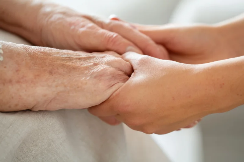 Elderly woman's hands gently held by a caregiver's hands in a close-up view