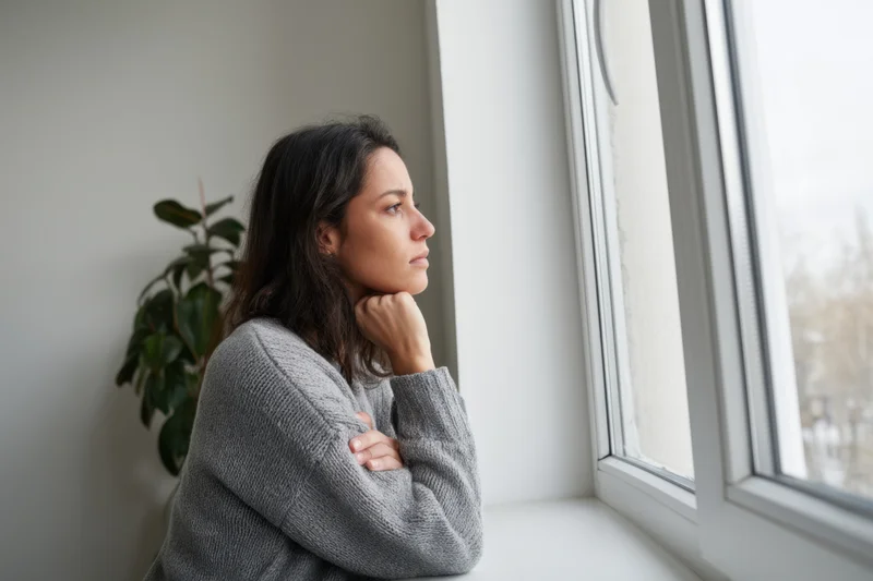 Woman in gray sweater sitting by window looking outside in quiet contemplation