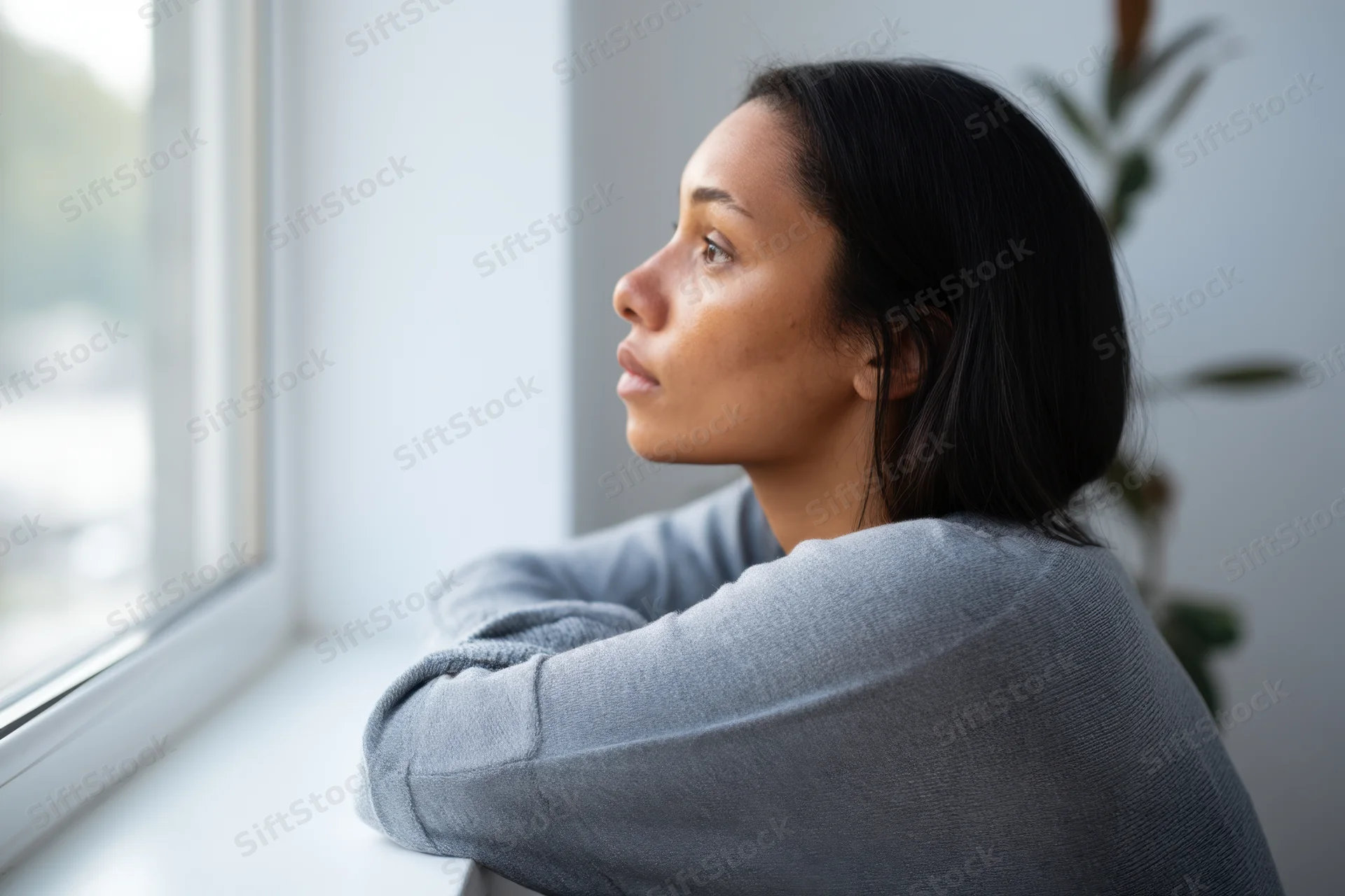 Woman in gray sweater leaning on windowsill looking out the window