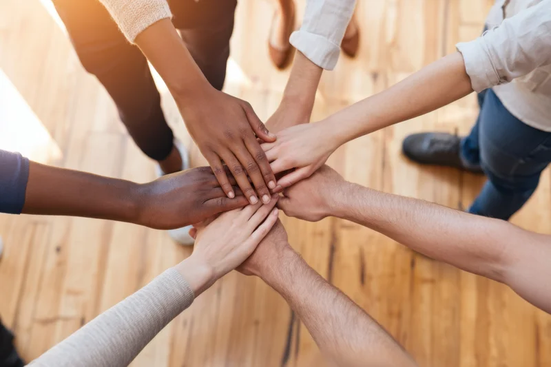 Diverse hands stacked together in a circle on wooden floor