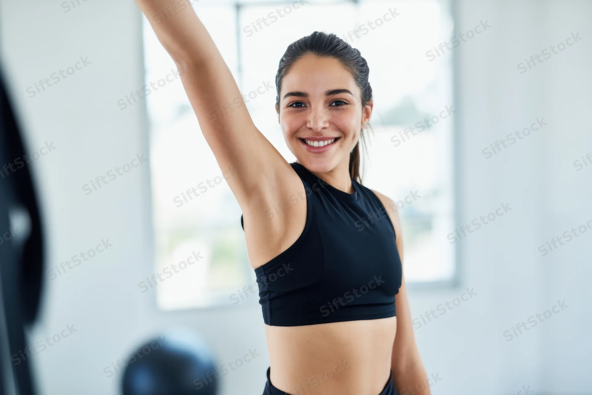 Woman stretching arm while smiling in a bright gym