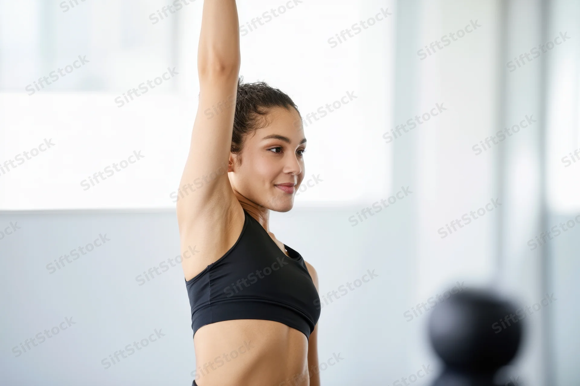Woman stretching arm upward in bright gym space