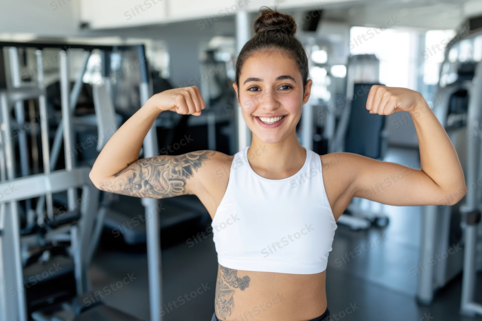 Woman flexing biceps in gym wearing white sports bra