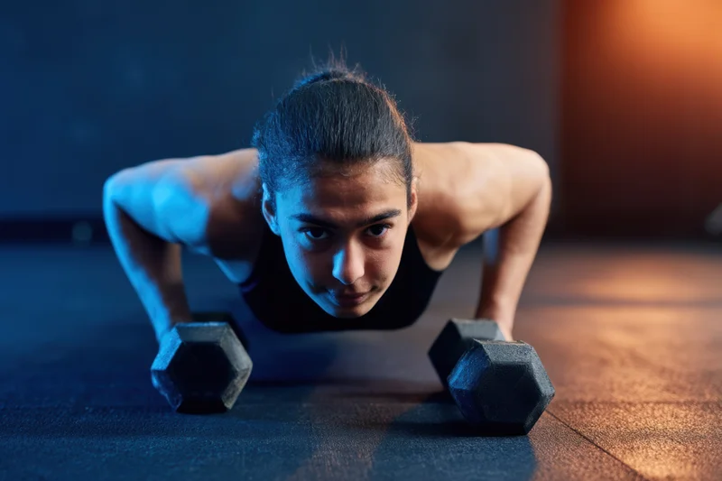 Woman doing weighted pushup with dumbbells on gym floor