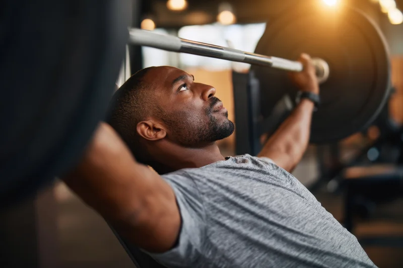 Man performing bench press with barbell in gym