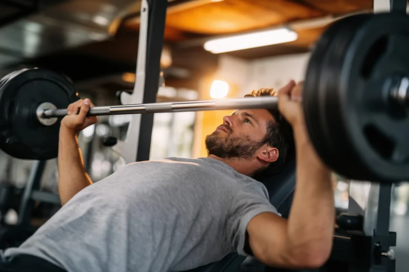 Man performing bench press with barbell in gym