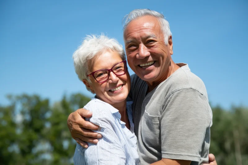 Elderly couple embracing and smiling outdoors on a sunny day
