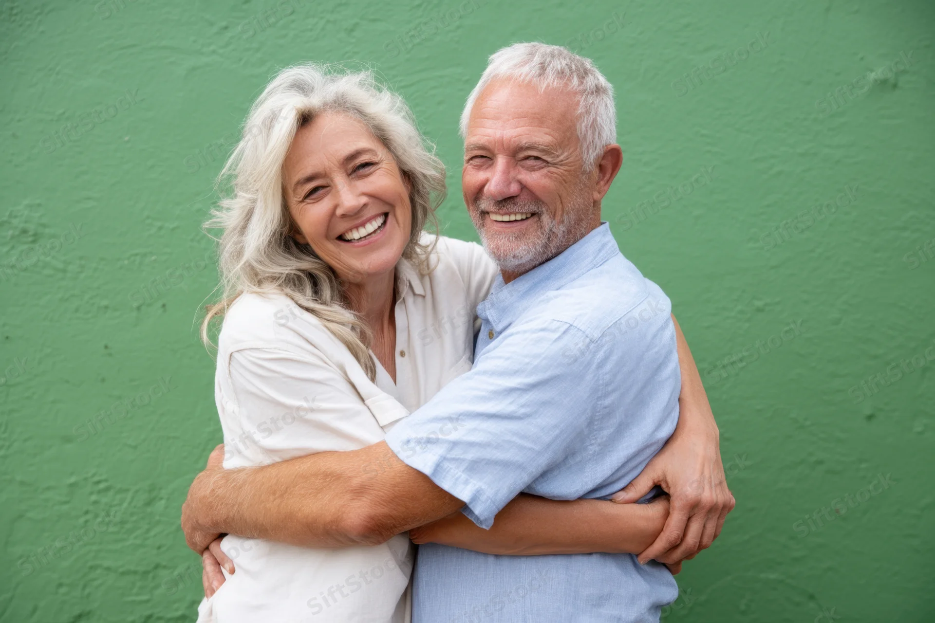 Elderly couple hugging and smiling against a green textured wall