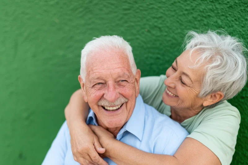 Elderly couple hugging and smiling against a green textured wall
