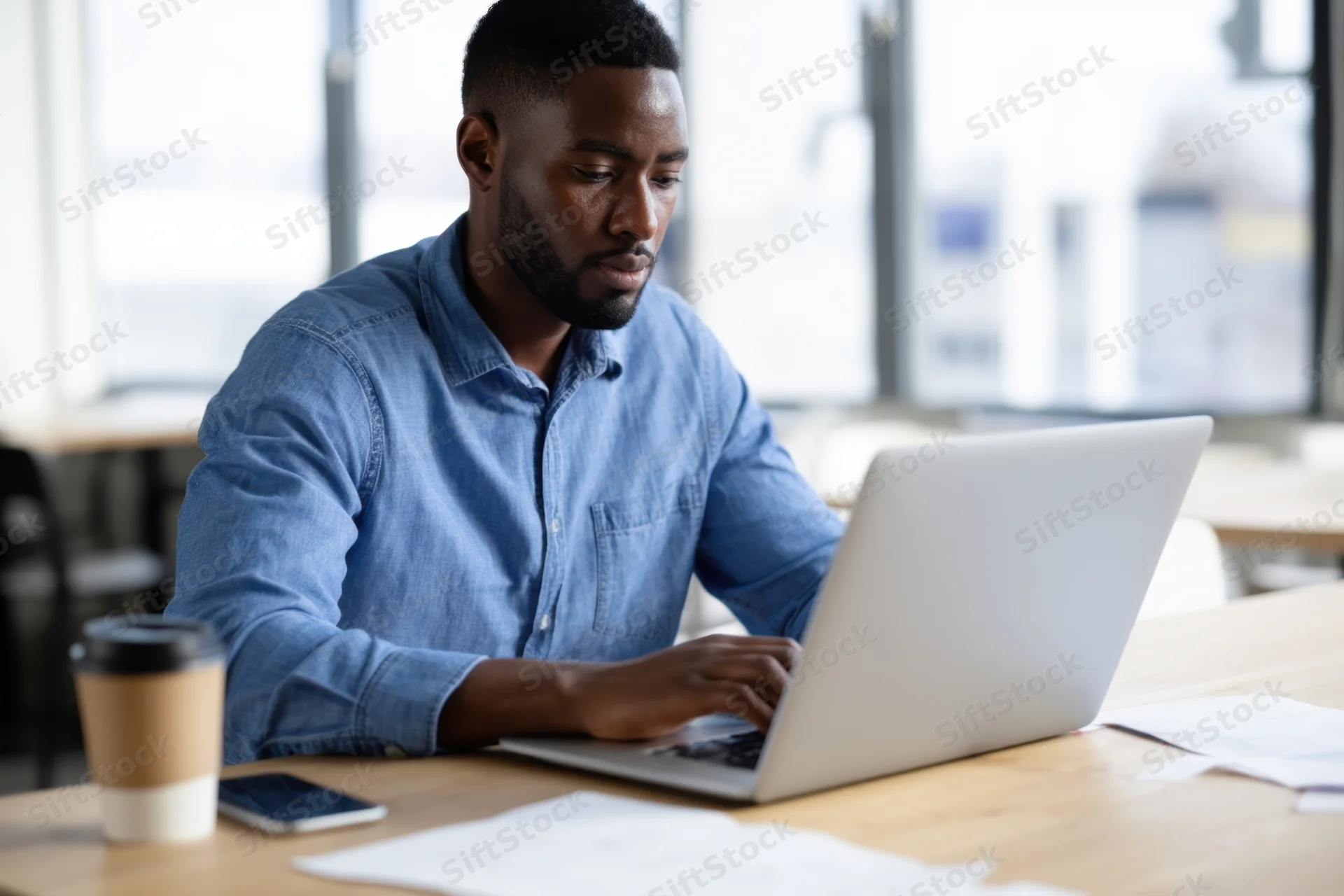 Man typing on laptop at wooden desk in office workspace